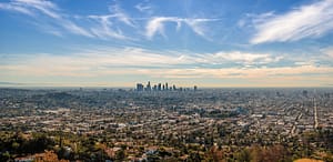 Panoramic view of Los Angeles with downtown skyscrapers in the distance under a blue sky with clouds.