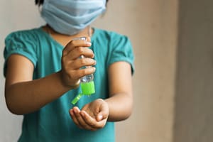 child wearing mask using hand sanitizer