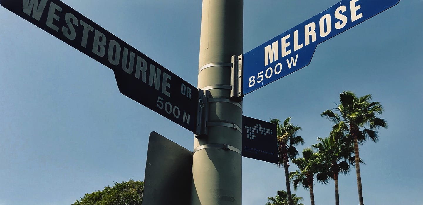 Street signs of Westbourne Drive and Melrose Avenue with palm trees in the background.